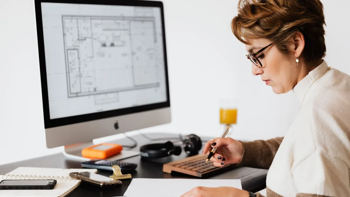 A person reviewing printed plans and documents at a desk with a computer