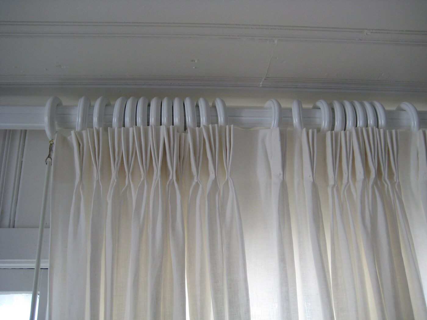A close view of a pinch pleat curtain heading hanging from rings on a white pole