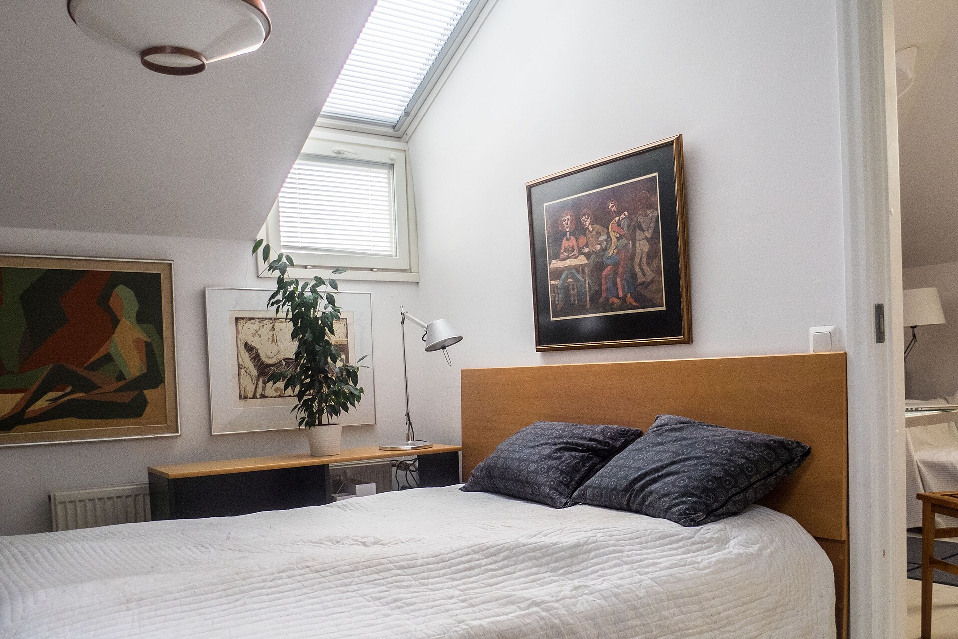 A styled attic bedroom with the bed tucked under the sloped ceiling next to a window
