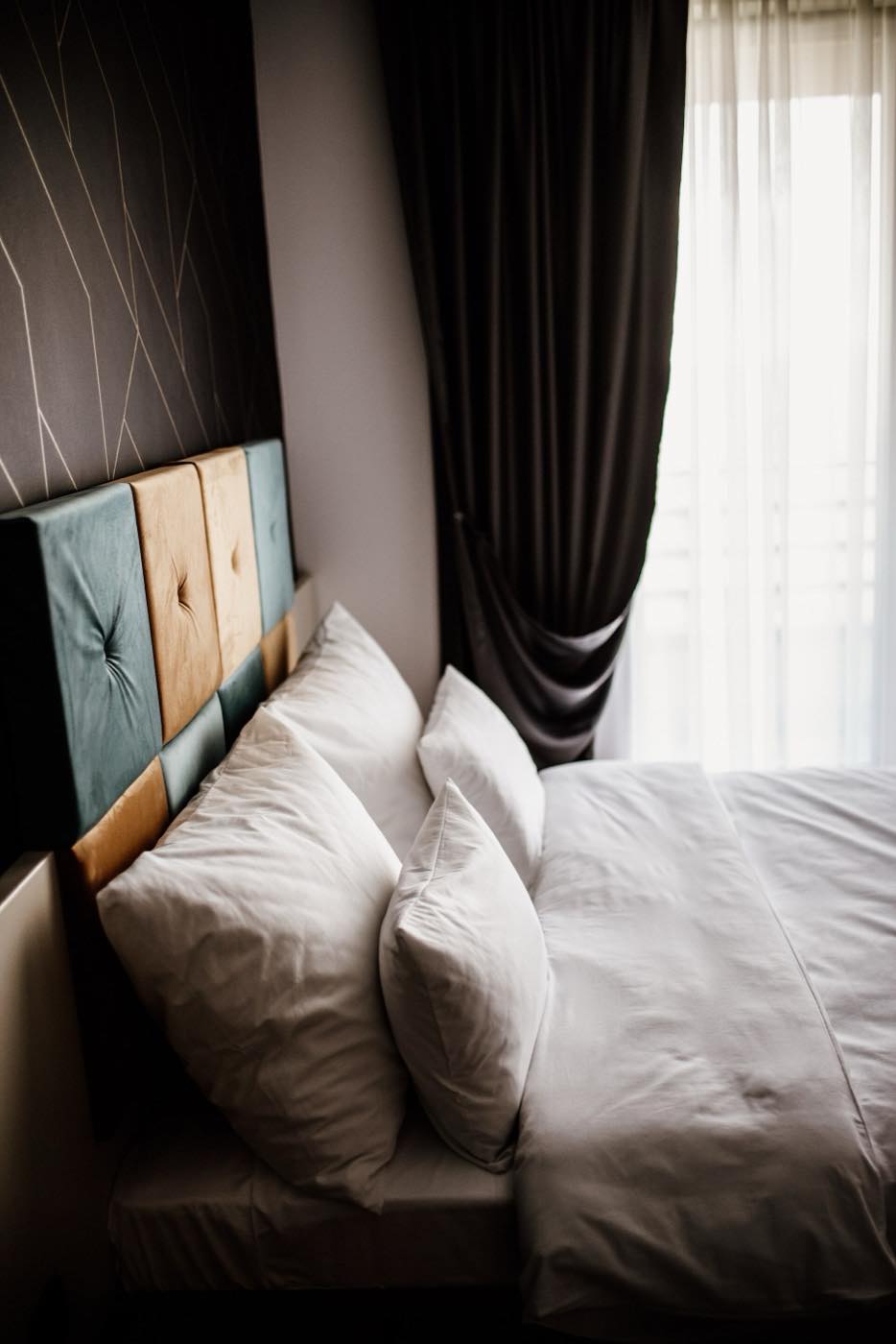 A bedroom with a dark wall in shadow next to a bright window with sheer curtains