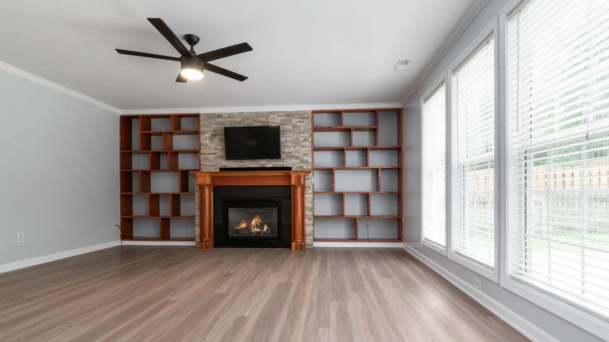 An empty unfurnished living room with large windows and hardwood floors in bright daylight