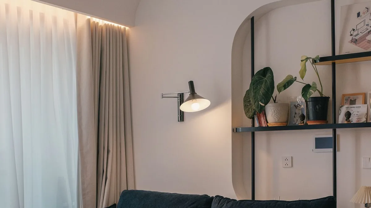 A cosy staged living-room corner with a navy sofa, warm lighting, sheer curtains, and styled shelving