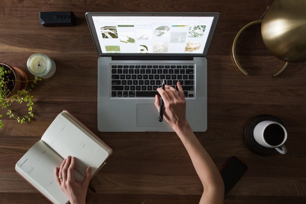 A person at a laptop with a notebook and a cup of coffee nearby