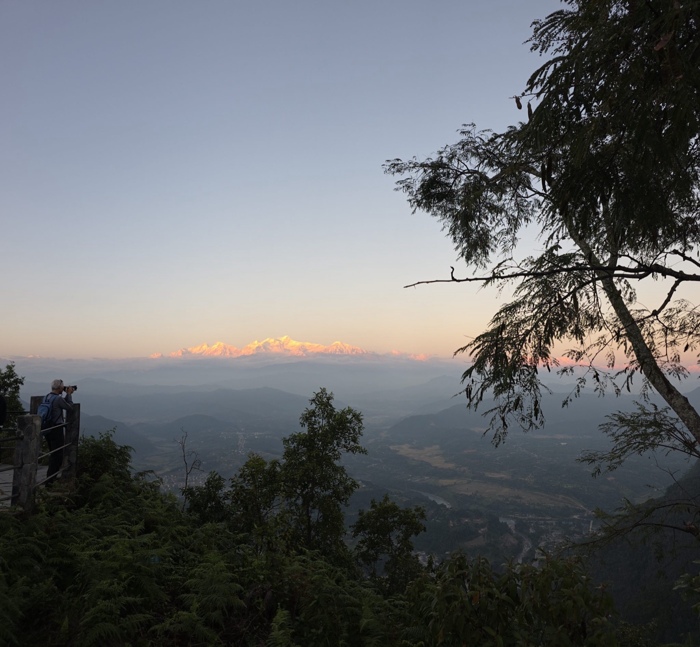 A person on a viewing platform looking out over mountains at sunrise