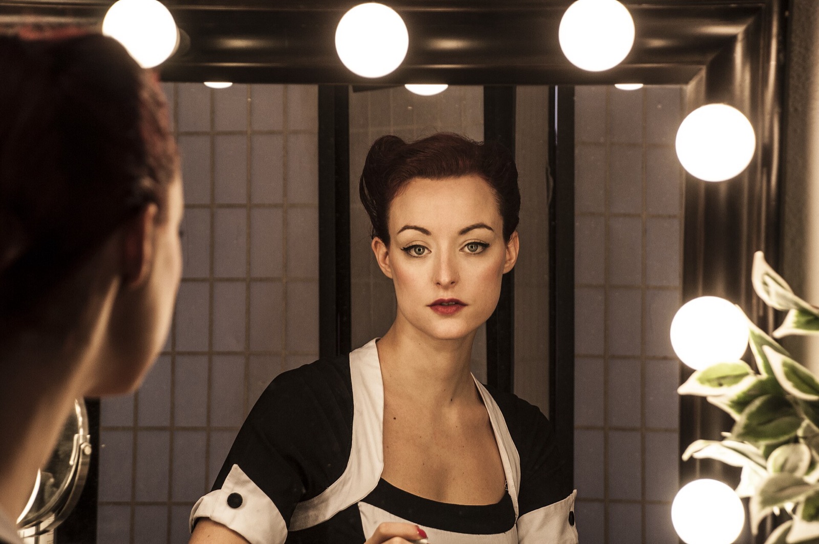 A woman looking at her reflection in a lit dressing room mirror