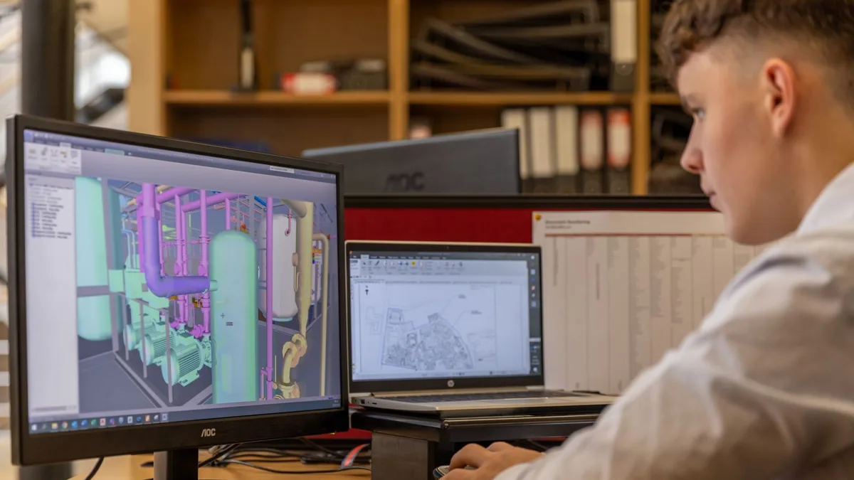 A drafting workstation with two large monitors displaying clean technical line drawings in a modern engineering studio