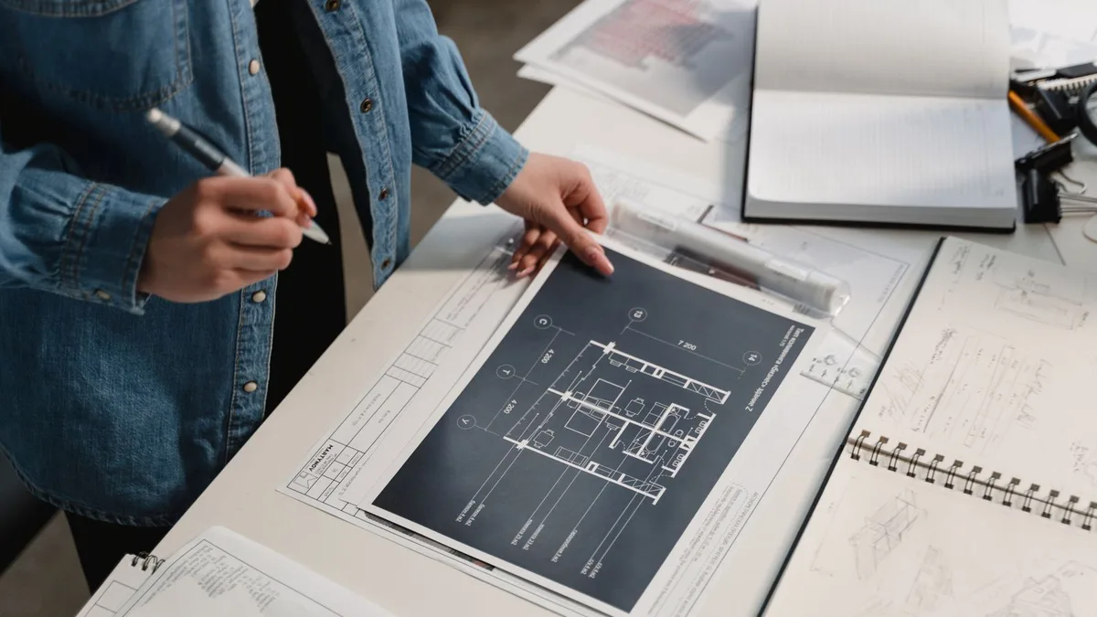 An engineer in a modern studio reviewing a printed technical drawing held in hand, with calipers and a laptop on the desk